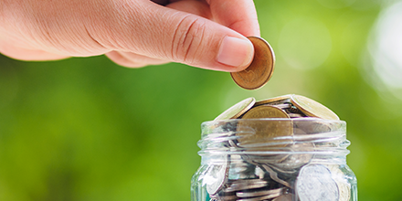 A person's hand placing coins into a jar symbolizing saving small amounts of money.