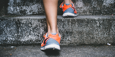 A person's feet wearing running shoes while walking up a flight of stairs.