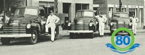 Servus's 80th anniversary theme image: Vintage photo of three men, each standing next to a 1930's pick-up truck.