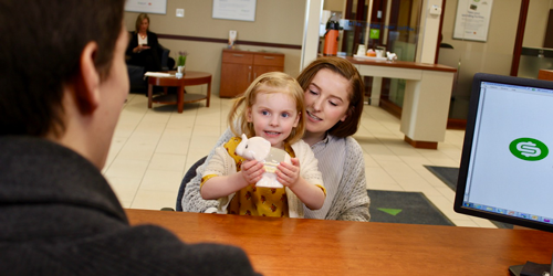 Hannah and her eldest daughter sitting at a desk with a Financial Advisor. The little girl holds an elephant piggy bank. 