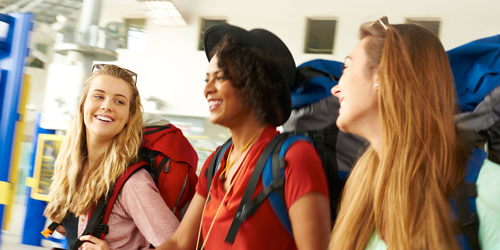 A group of three women in their 20's have backpacks on and are ready to go on a trip. 